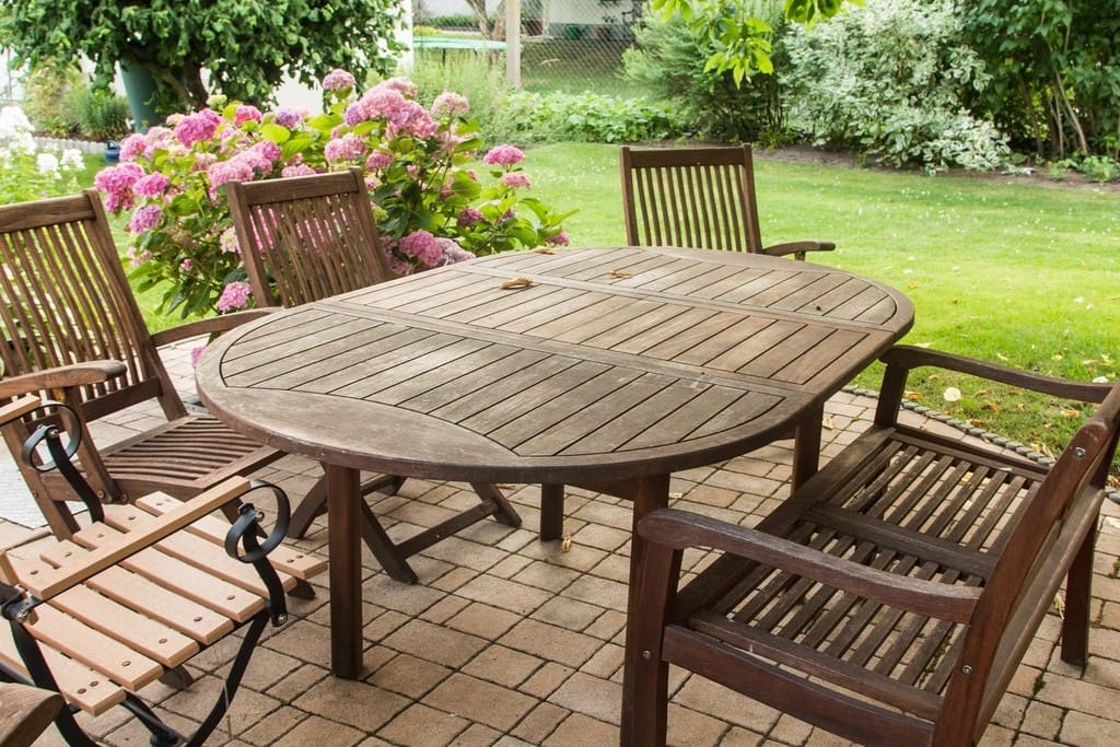 Wooden dining set on a brick paver patio beside a lawn and hydrangeas